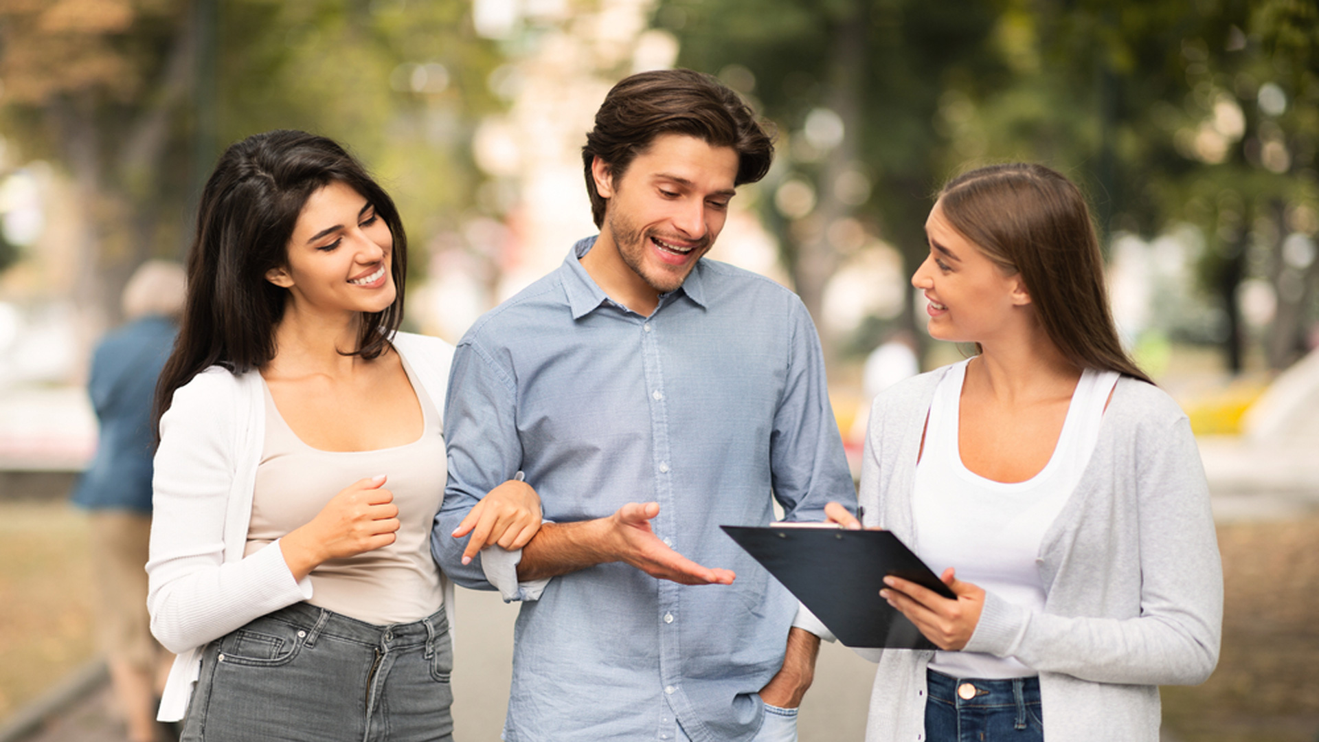Utomhusbild med tre personer som samtalar och tittar på en iPad