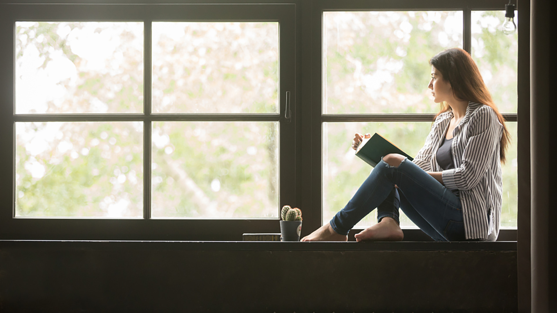 Kvinna sitter på en fönsterbänk och läser en bok
